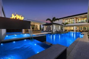 Photo taken in the backyard 1292 grand traverse pkwy, a $12.5M Reunion Resort Mansion. The photo primarily features the swimming pool at dusk with the lights turned on.