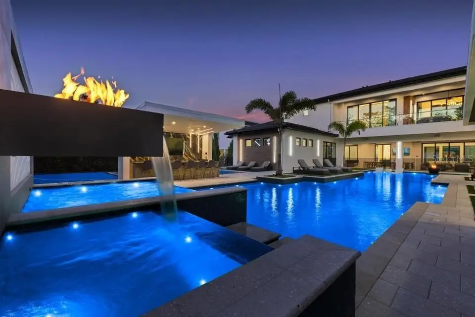 Photo taken in the backyard 1292 grand traverse pkwy, a $12.5M Reunion Resort Mansion. The photo primarily features the swimming pool at dusk with the lights turned on.